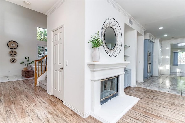 living room featuring built in features, ornamental molding, and light wood-type flooring