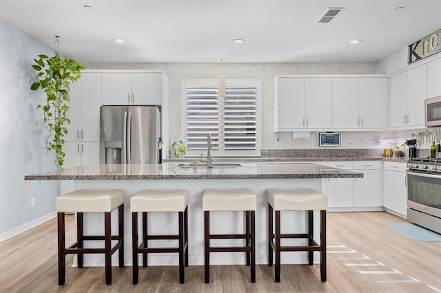 kitchen featuring light hardwood / wood-style floors, a kitchen bar, white cabinetry, and stainless steel appliances