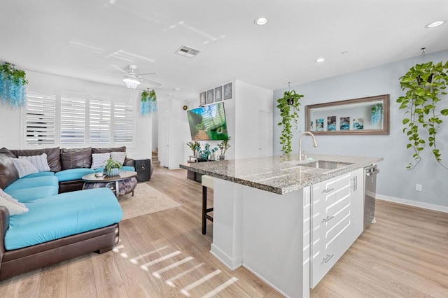 kitchen featuring light stone countertops, light wood-type flooring, sink, white cabinetry, and an island with sink