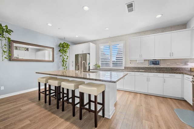 kitchen with sink, stainless steel refrigerator with ice dispenser, an island with sink, white cabinets, and light wood-type flooring