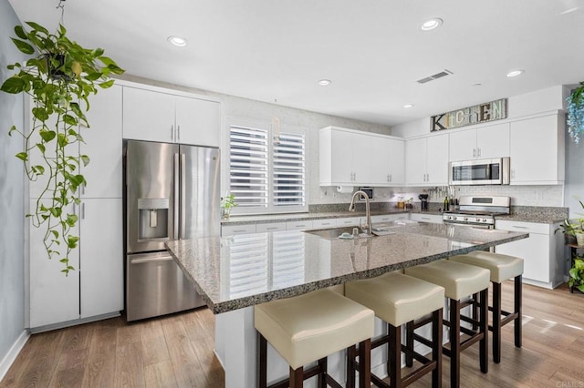 kitchen featuring sink, stainless steel appliances, light hardwood / wood-style floors, a center island with sink, and white cabinets