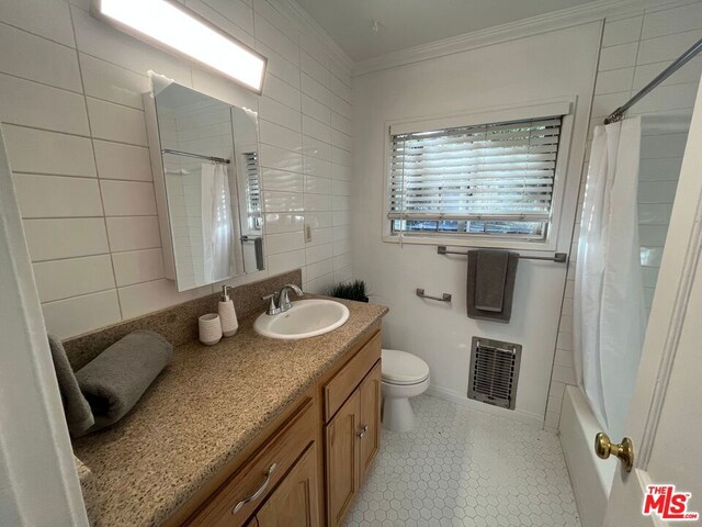 full bathroom featuring vanity, toilet, shower / bath combo with shower curtain, ornamental molding, and tile walls