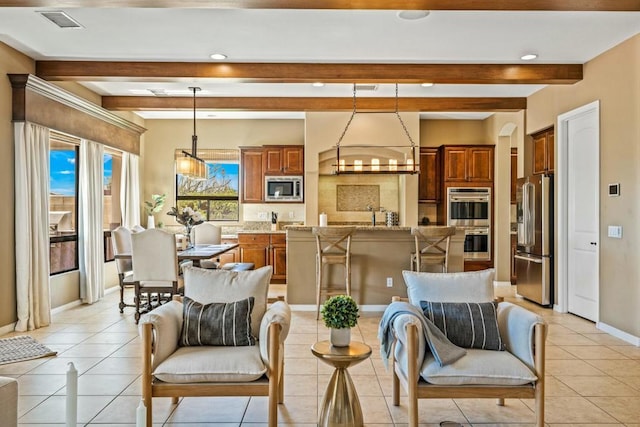 interior space featuring beam ceiling, a center island, decorative light fixtures, light tile patterned flooring, and appliances with stainless steel finishes