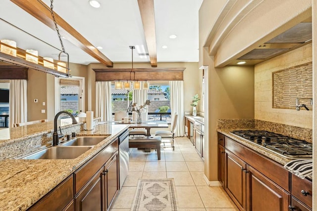 kitchen with beamed ceiling, light stone counters, hanging light fixtures, and sink