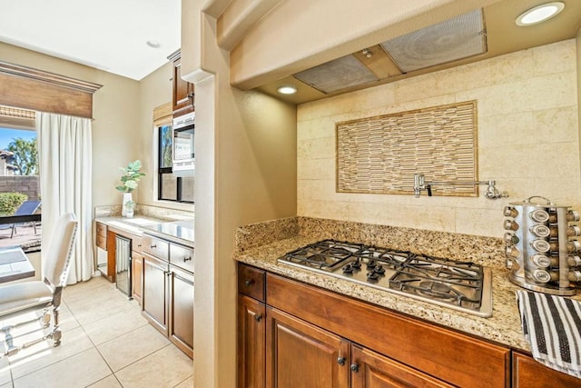 kitchen featuring light stone countertops, tile walls, stainless steel gas stovetop, and light tile patterned flooring