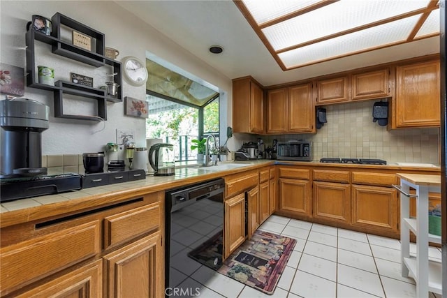 kitchen with tasteful backsplash, sink, black appliances, light tile patterned floors, and tile counters