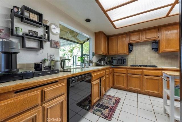 kitchen featuring tile countertops, a sink, dishwasher, open shelves, and brown cabinetry