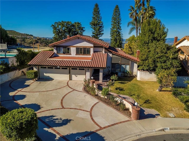 mediterranean / spanish-style house featuring a garage, driveway, a tiled roof, fence, and a front yard