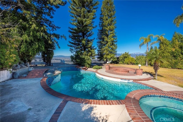 pool with a patio area, a mountain view, and an in ground hot tub