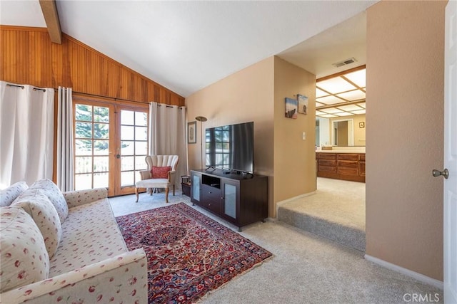 carpeted living room featuring wooden walls, french doors, and lofted ceiling with beams