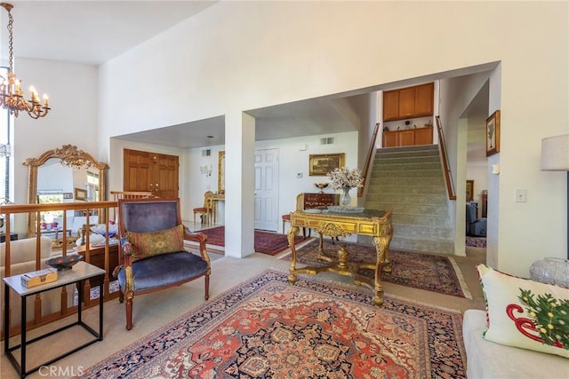 living area with light colored carpet, visible vents, a high ceiling, a chandelier, and stairs