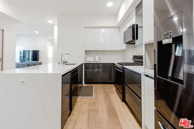 kitchen with white cabinetry, sink, kitchen peninsula, light hardwood / wood-style floors, and appliances with stainless steel finishes