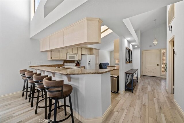 324 Sundance Cir, Palm Desert, CA 92211 - kitchen with light stone countertops, kitchen peninsula, white appliances, light hardwood / wood-style flooring, and high vaulted ceiling