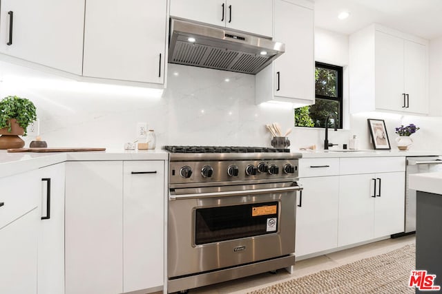 kitchen with decorative backsplash, premium range, sink, light tile patterned floors, and white cabinets