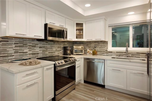 kitchen with sink, stainless steel appliances, tasteful backsplash, light hardwood / wood-style floors, and white cabinets