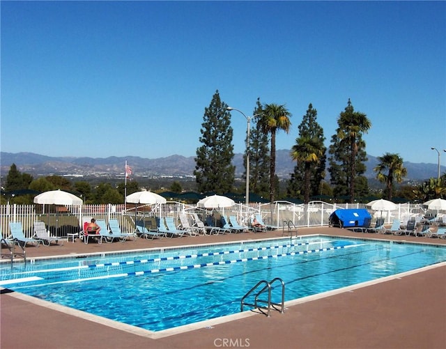 community pool featuring a mountain view, a patio, and fence