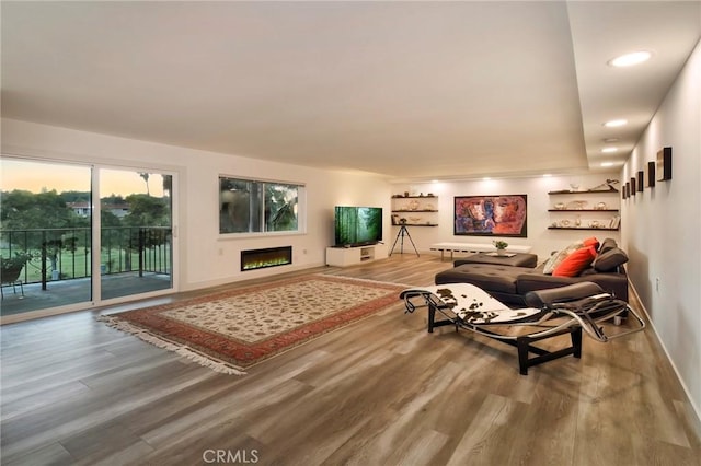 living area featuring recessed lighting, a warm lit fireplace, baseboards, and wood finished floors