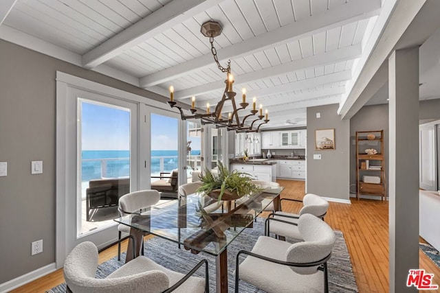 dining space featuring a chandelier, beam ceiling, a water view, and light hardwood / wood-style floors