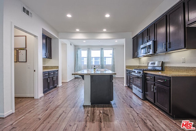 kitchen with light stone countertops, a kitchen island with sink, appliances with stainless steel finishes, and light hardwood / wood-style flooring