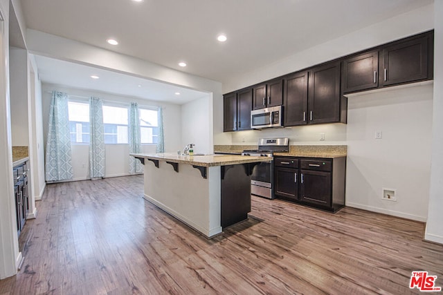 kitchen featuring dark brown cabinetry, stainless steel appliances, light hardwood / wood-style flooring, an island with sink, and a breakfast bar area