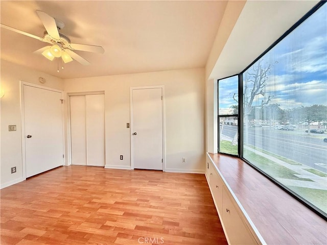 interior space with access to exterior, light wood-type flooring, ceiling fan, and multiple closets