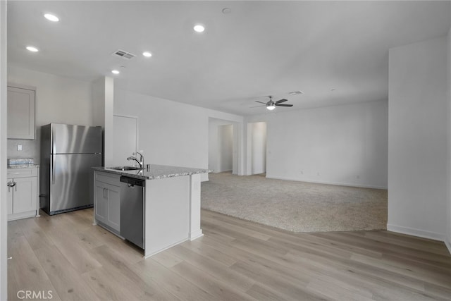 kitchen featuring a center island with sink, sink, ceiling fan, light wood-type flooring, and appliances with stainless steel finishes