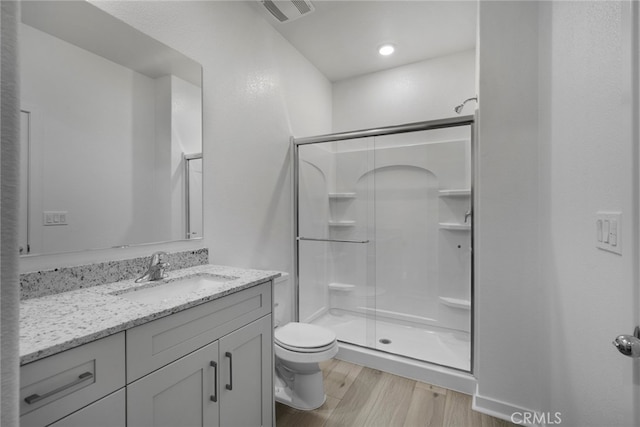 bathroom with a shower with door, vanity, wood-type flooring, and toilet