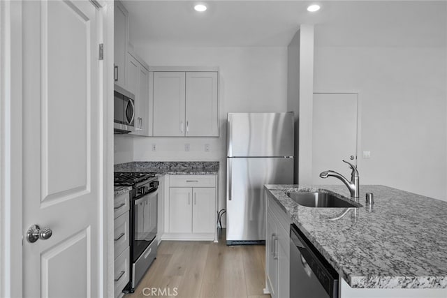 kitchen with white cabinetry, sink, stainless steel appliances, light stone counters, and light wood-type flooring