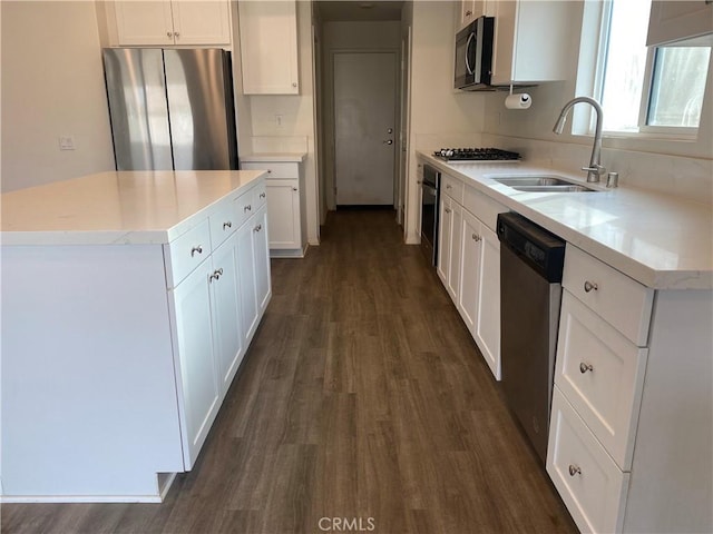 kitchen with appliances with stainless steel finishes, sink, white cabinets, dark hardwood / wood-style floors, and a kitchen island