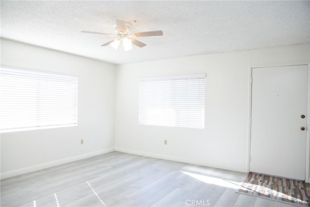 unfurnished room with ceiling fan, light wood-type flooring, a textured ceiling, and a wealth of natural light