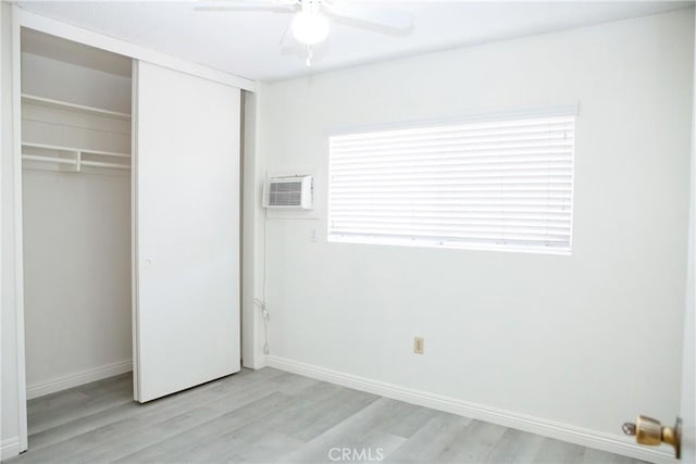 unfurnished bedroom featuring a wall mounted AC, light wood-type flooring, a closet, and ceiling fan