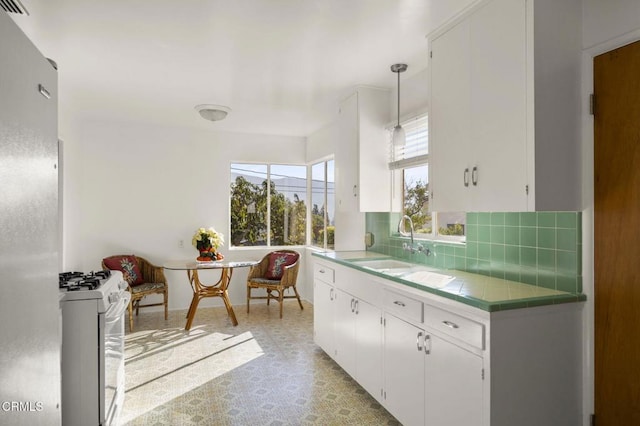 kitchen with decorative backsplash, sink, white cabinetry, hanging light fixtures, and white gas stove