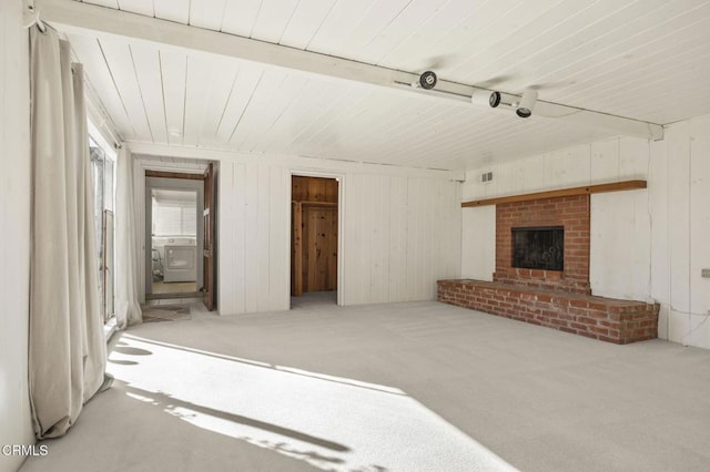 unfurnished living room with carpet flooring, a brick fireplace, wooden walls, beamed ceiling, and washer / clothes dryer