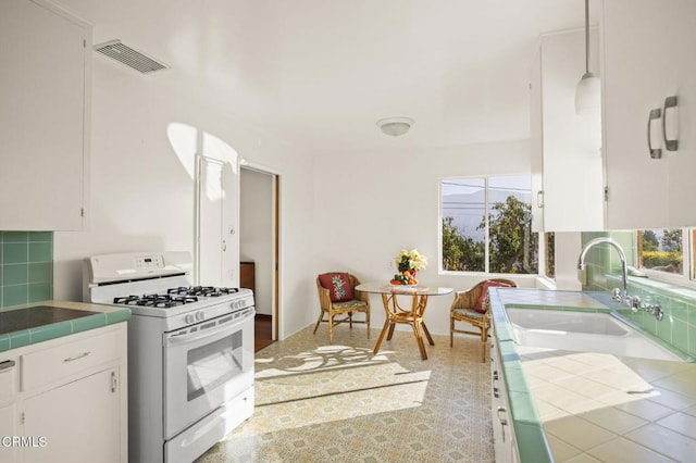 kitchen featuring white range with gas stovetop, visible vents, tile countertops, and white cabinets