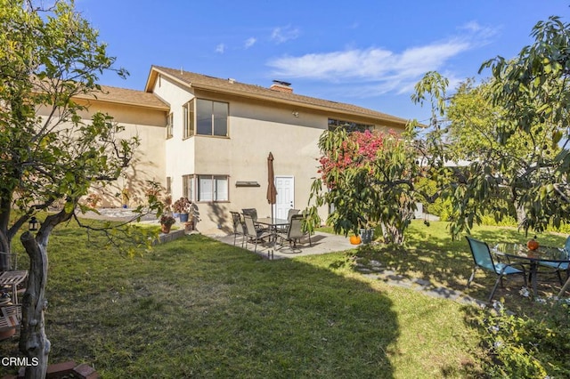 rear view of property featuring stucco siding, a chimney, a lawn, and a patio