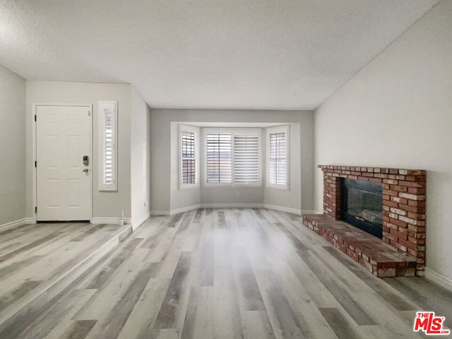 unfurnished living room featuring light hardwood / wood-style floors, a textured ceiling, and a brick fireplace