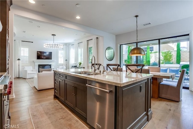 kitchen featuring stainless steel dishwasher, a kitchen island with sink, sink, and pendant lighting