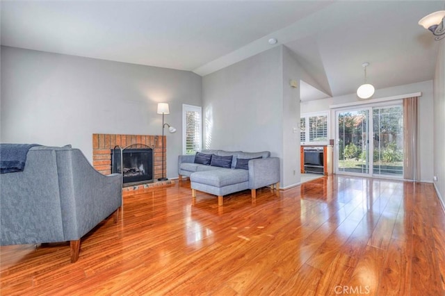 living room featuring wood-type flooring, vaulted ceiling, and a brick fireplace