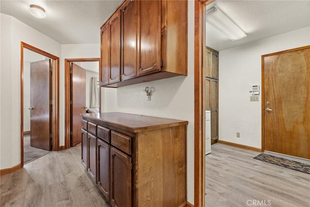 kitchen featuring dark countertops, baseboards, light wood-style flooring, brown cabinets, and a textured ceiling