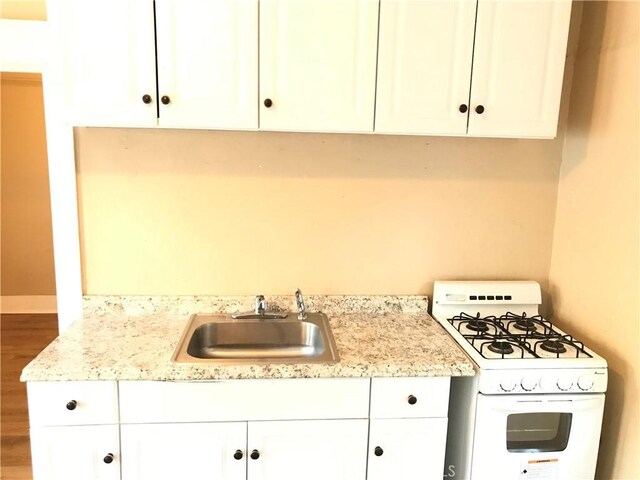 kitchen with light stone countertops, sink, wood-type flooring, white cabinetry, and white gas stove