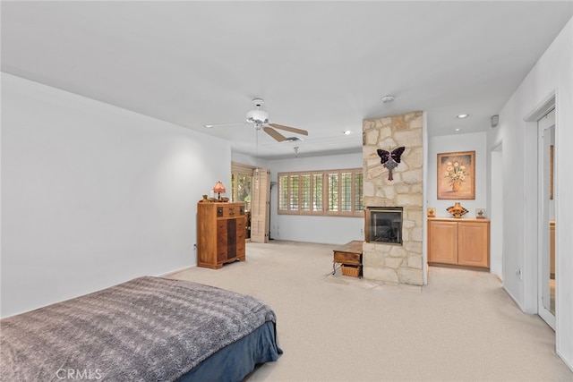 bedroom with ceiling fan, light colored carpet, and a stone fireplace