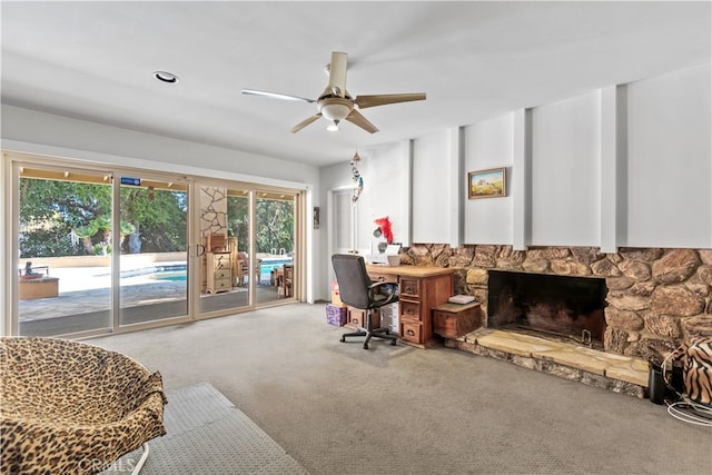 home office featuring carpet floors, ceiling fan, and a stone fireplace