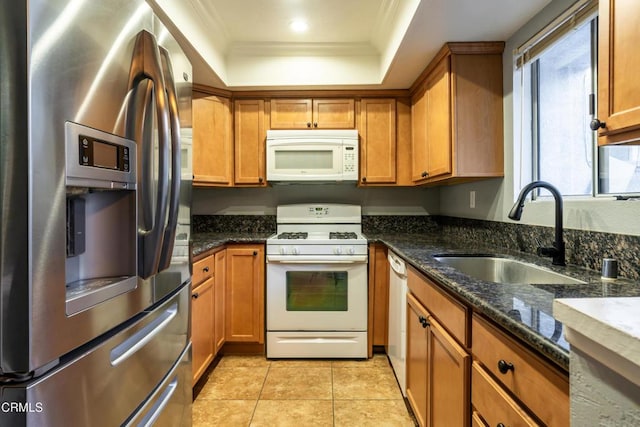 kitchen featuring sink, dark stone countertops, white appliances, a tray ceiling, and light tile patterned floors