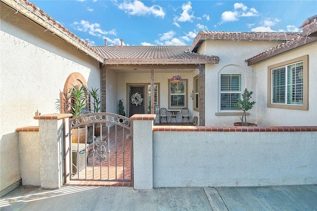 view of exterior entry featuring a porch, a gate, fence, and stucco siding