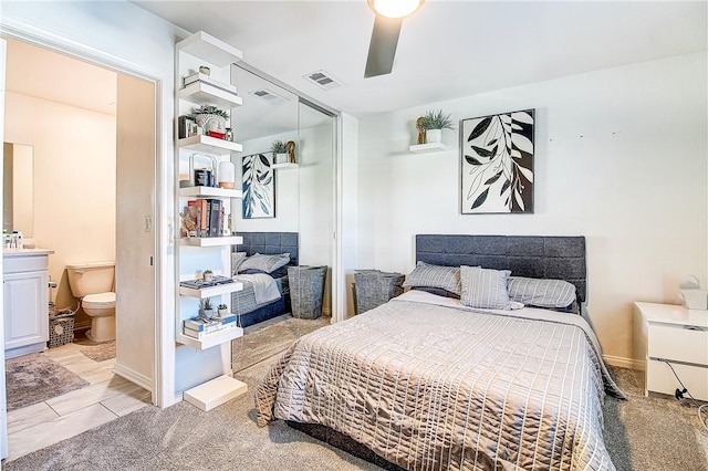 bedroom with ceiling fan, ensuite bathroom, and light carpet