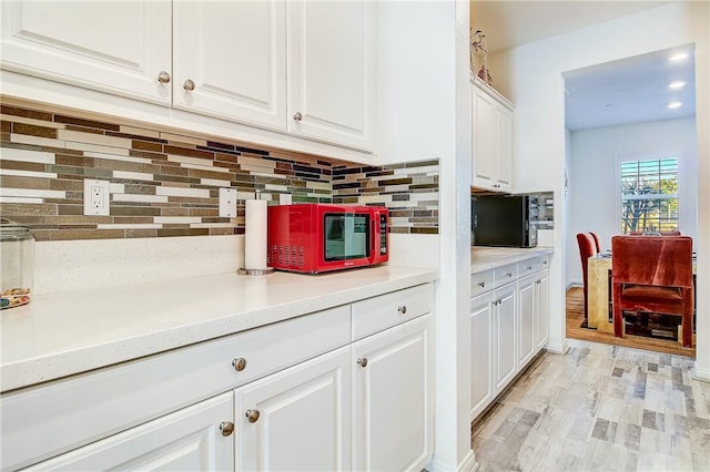 kitchen with decorative backsplash, white cabinetry, and light wood-type flooring