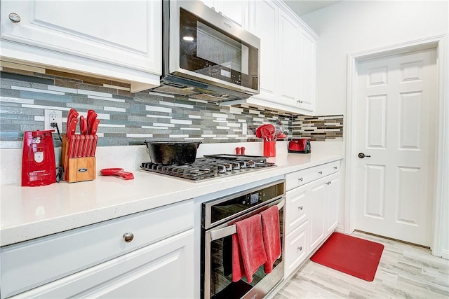 kitchen featuring backsplash, light wood-type flooring, white cabinetry, and stainless steel appliances