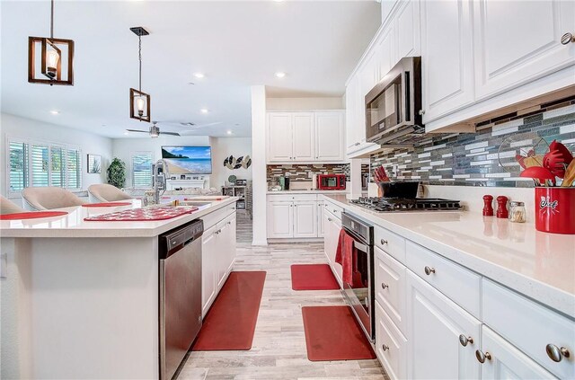 kitchen featuring white cabinetry, a center island, hanging light fixtures, light hardwood / wood-style floors, and appliances with stainless steel finishes