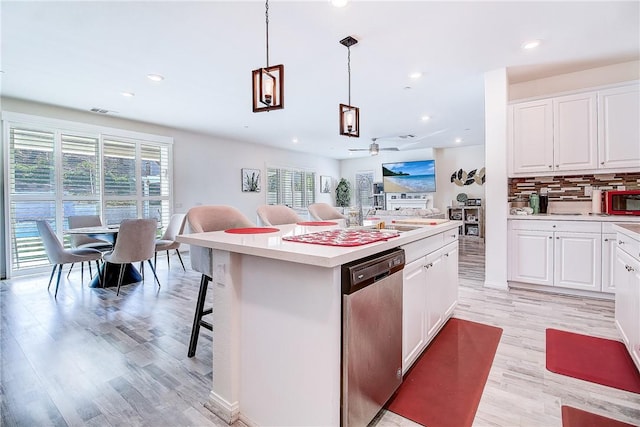 kitchen featuring a center island, decorative light fixtures, stainless steel dishwasher, and white cabinetry