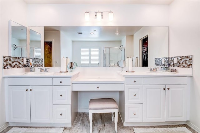 bathroom featuring vanity, wood-type flooring, a shower with door, and backsplash